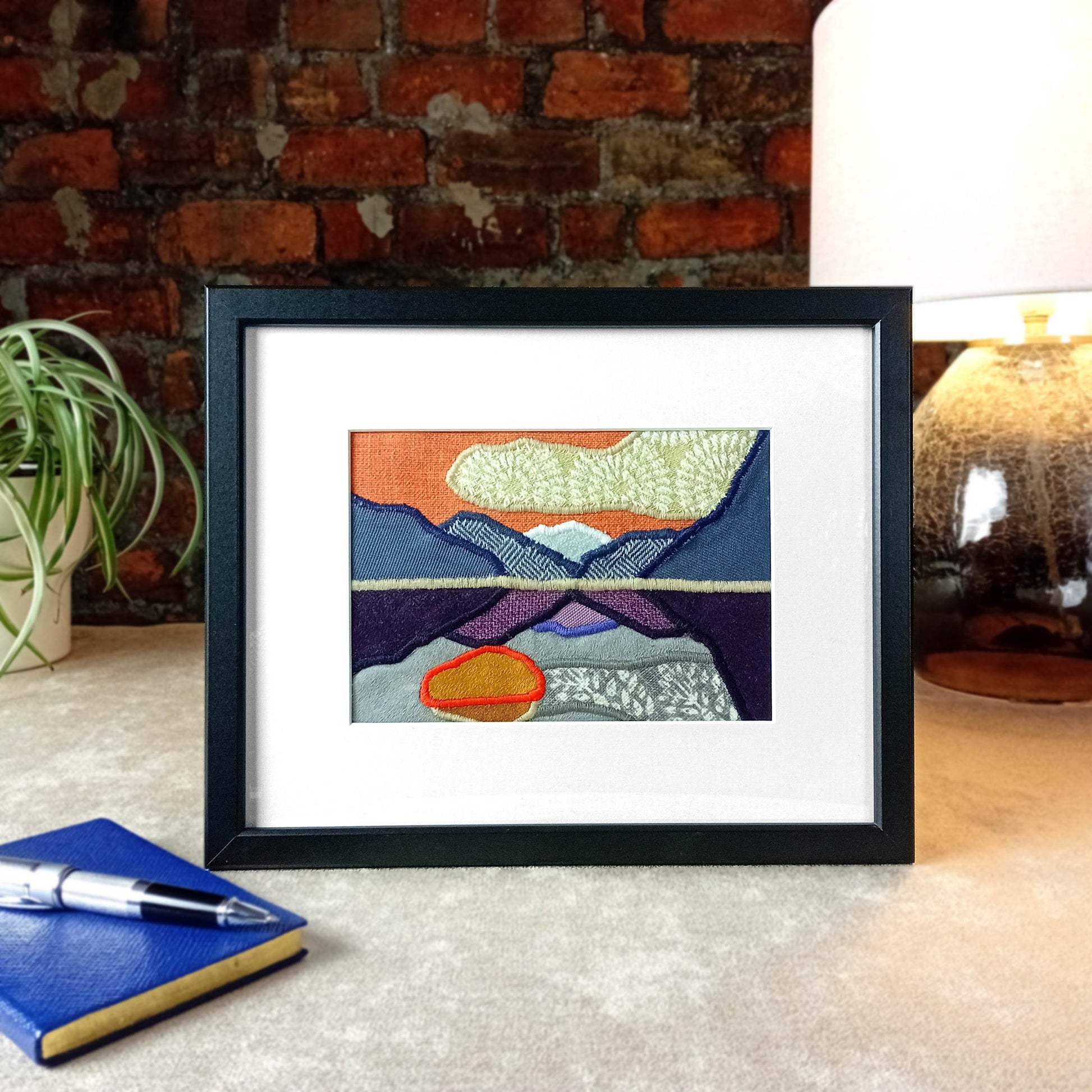 Framed fabric art with a mountain and lake scene