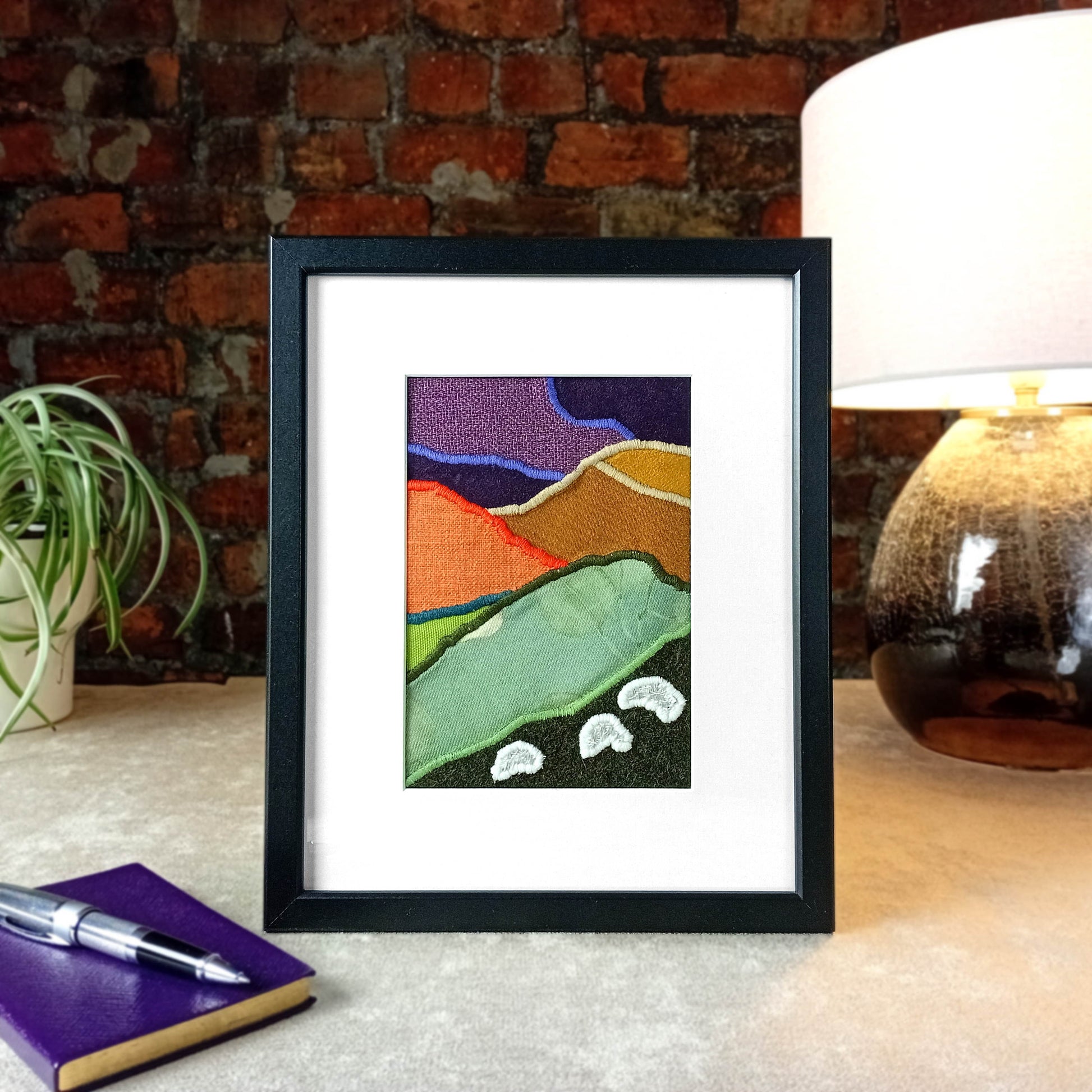 Framed fabric artwork with a hillside landscape featuring highland sheep