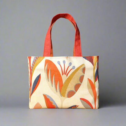 Small cotton tote bag with tulip pattern in shades of warm orange, rich ochre, and classic denim blue on an off-white background