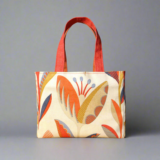 Small cotton tote bag with tulip pattern in shades of warm orange, rich ochre, and classic denim blue on an off-white background