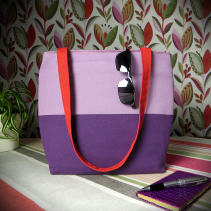 Large cotton tote bag with two vibrant colours on each side sitting on a table with a notebook, pen, and plant