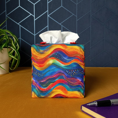 A colourful wave design square tissue box cover, a pen and notebook, and a plant.