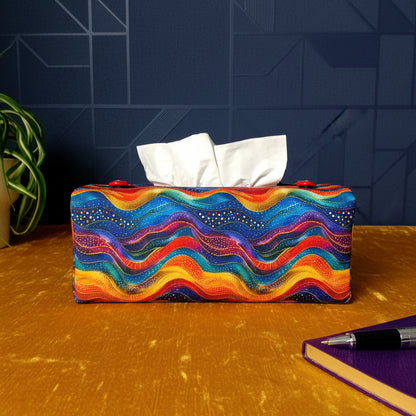 A colourful wave patterned rectangular tissue box, a pen and notebook, and a plant