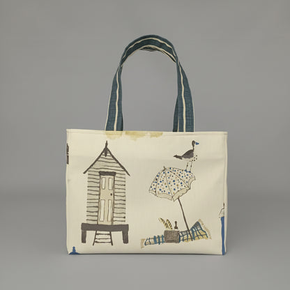 Back view of a handmade cotton mini tote bag patterned with a beach hut, beach blanket and beach umbrella illustrations on an off-white background.