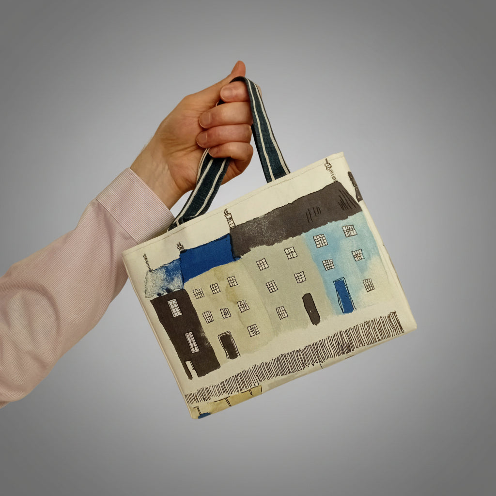 A hand holding the cotton mini tote bag with seaside and beach themed illustrations on an off-white background.