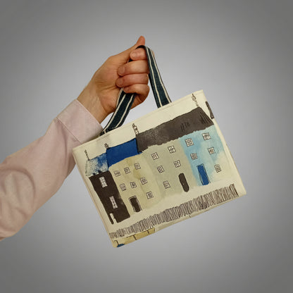 A hand holding the cotton mini tote bag with seaside and beach themed illustrations on an off-white background.