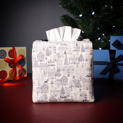 Square tissue box cover with holiday themed winter village scene on off-white background with Christmas themed decor