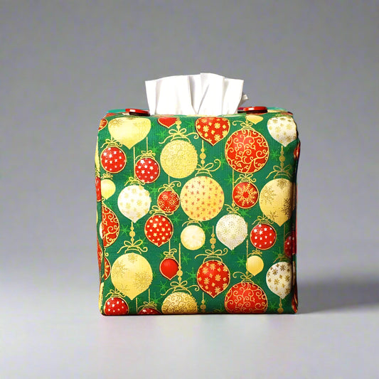 Square tissue box cover with holiday themed red, gold, and white Christmas baubles with metallic gold accent on green background