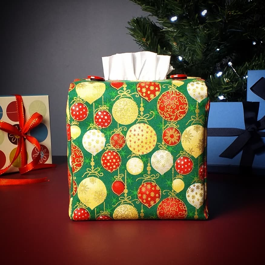 Square tissue box cover with holiday themed red, gold, and white Christmas baubles with metallic gold accent on green background with Christmas themed decor