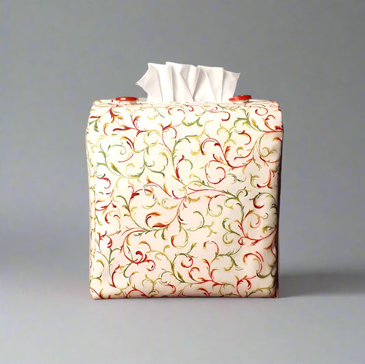 Square tissue box cover with holiday themed red and green swirls with metallic gold accent on cream colour background