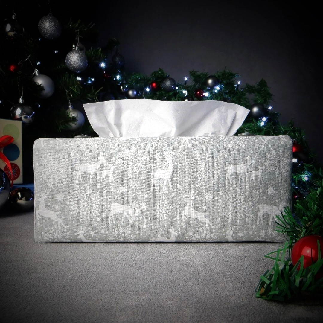 Rectangular tissue box cover with holiday themed white reindeer design on grey background with Christmas themed decorations