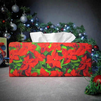 Rectangular tissue box cover with holiday themed poinsettia design on green leaf pattern background with Christmas themed decorations