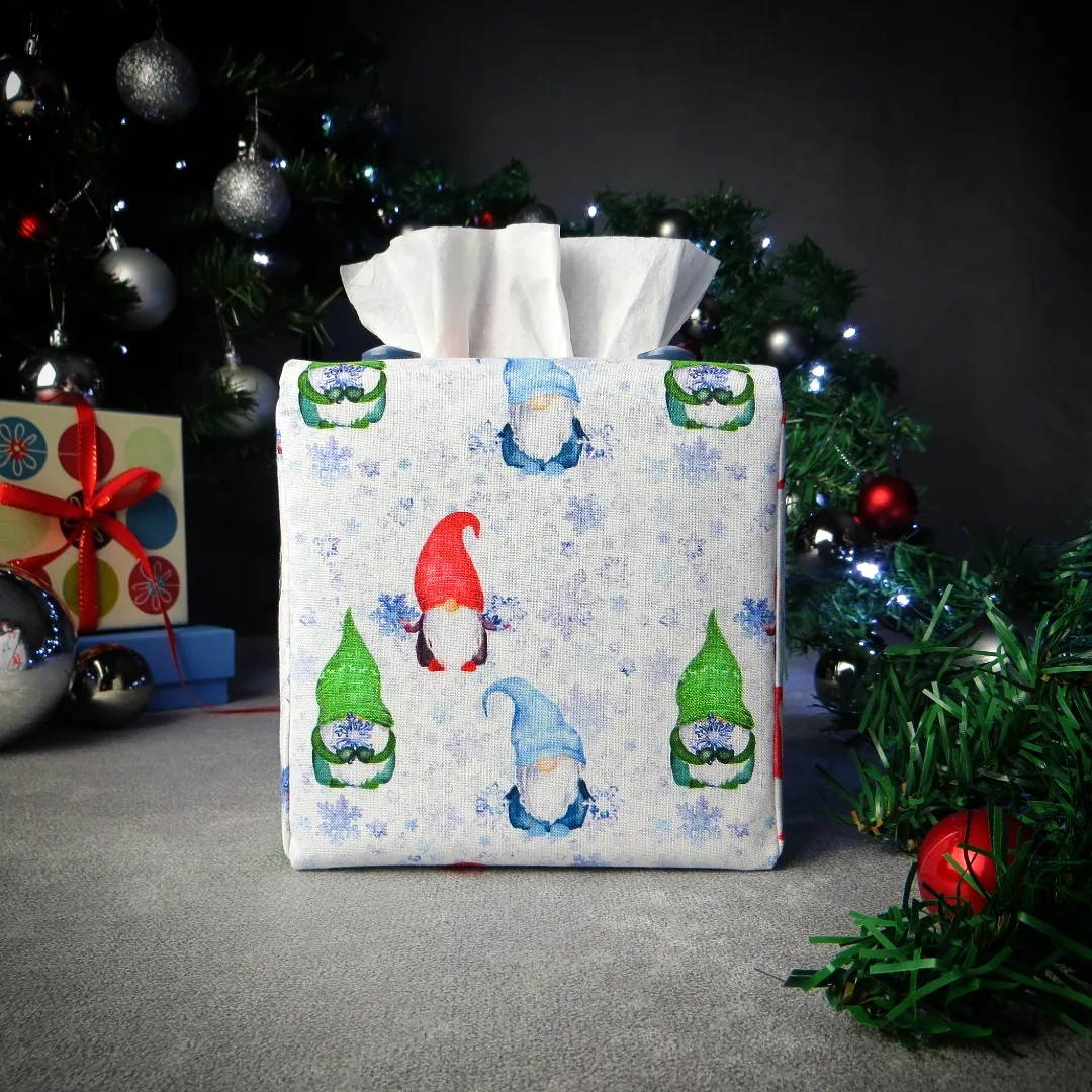 Square tissue box cover with holiday themed red, green, and blue gnomes design on white and blue snowflake pattern background with Christmas themed decor