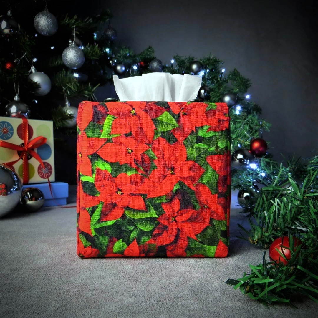 Square tissue box cover with holiday themed poinsettia design on green leaf pattern background with Christmas themed decor