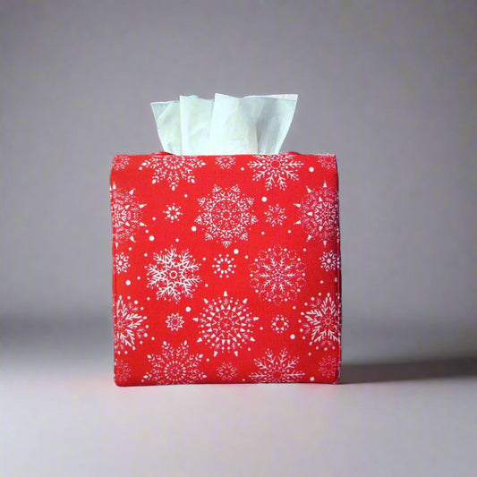 Square tissue box cover with holiday themed white snowflakes design on red background