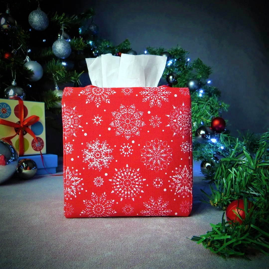 Square tissue box cover with holiday themed white snowflakes design on red background with Christmas themed decor