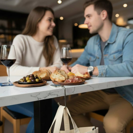 A glass and metal handbag hook hanging on a restaurant table to suspend a tote bag off of the floor
