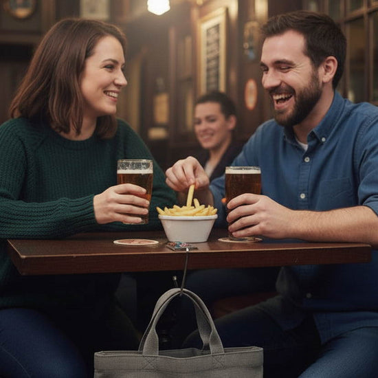 A glass and metal handbag hook on a pub table suspending a tote bag from the touching the floor